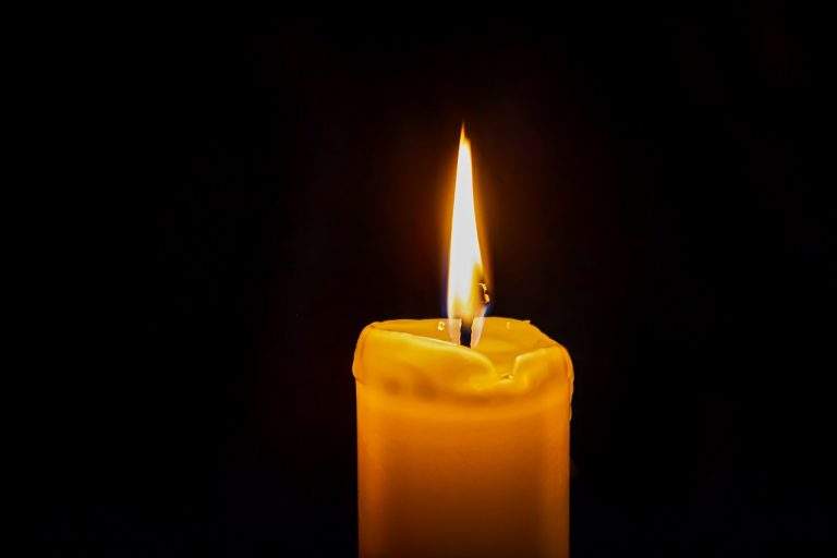 Eine orange Kerze brennt mit ruhiger Flamme vor einfarbig schwarzem Hintergrund.