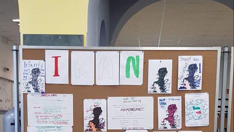 Eine Stellwand im Schulfoyer ist zu sehen. Darauf handgefertigte Bilder und Texte, zum Beispiel der Schriftzug "Frau-Leben-Freiheit" oder Bilder von verzweifelten Frauenköpfen und dem Text "Help Iran".