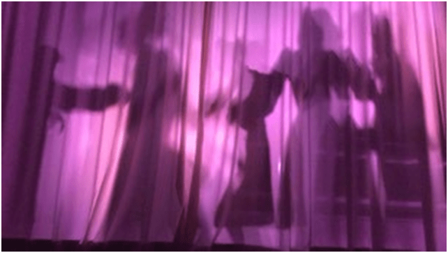 Unscharfe Schatten von Menschen sind hinter einem lila beleuchteten Vorhang zu sehen.