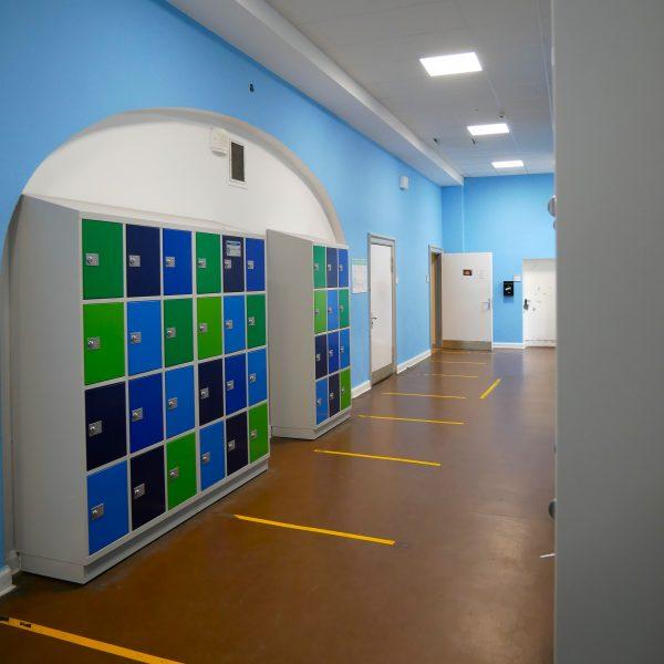 Moderne, gut gewartete Spinde in freundlichen Farben stehen in den hellblau gestrichenen Schulfluren.