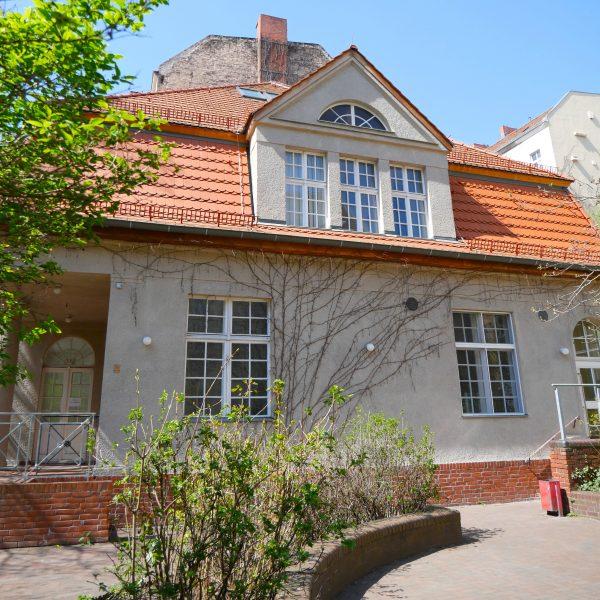 Ein kleines Gebäude mit weißen Sprossenfenstern im Erdgeschoss und einem Dachgeschoss mit großer Gaube.