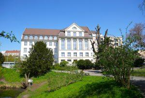 Unser heller Altbau mit weißen Sprossenfenstern und angedeuteten Säulen am grünen Fennsee-Park.