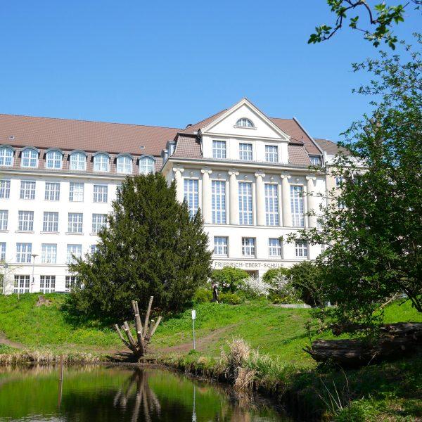 Unser freundlicher Altbau mit angedeuteten Säulen und weißen Sprossenfenstern am grünen Fennsee-Park.