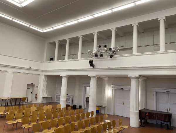 Klassizistische weiße Aula mit Säulen und umlaufender Galerie, ausgestattet mit modernster Beleuchtungstechnik.