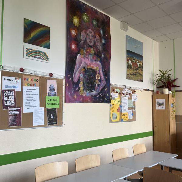 Neben einem großen, an eine hinduistische Göttin erinnernden Bild hängt die Psychologie-Pinwand mit den Plakaten "Hanau ist kein Einzelfall" und "Zeit zum Nachdenken". Außerdem Bilder von Regenbögen und von einer Meereslandschaft.