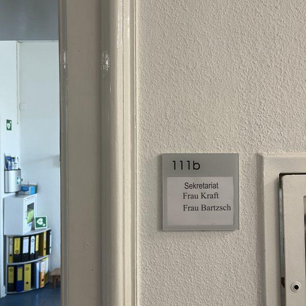 Eingangstür zum Sekretariat, mit dem Schild "Raum 111b: Sekretariat. Frau Kraft. Frau Bartzsch."