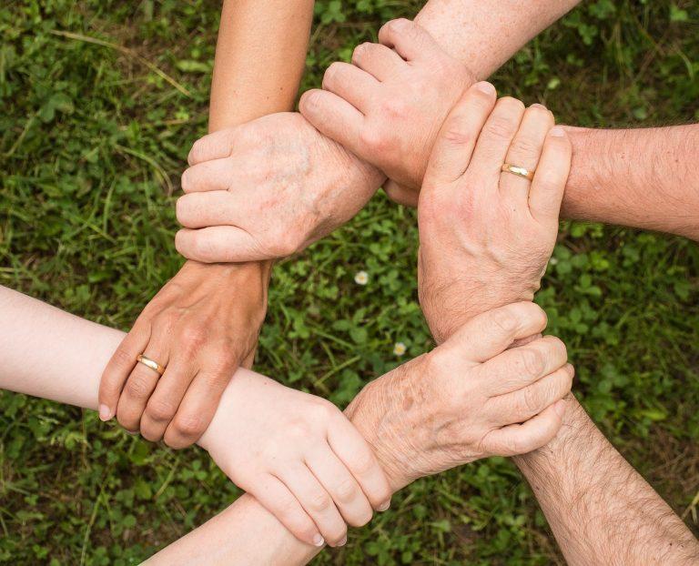 6 Menschen unterschiedlichen Alters und Geschlechts bilden mit Ihren Händen einen gemeinsamen Kreis.